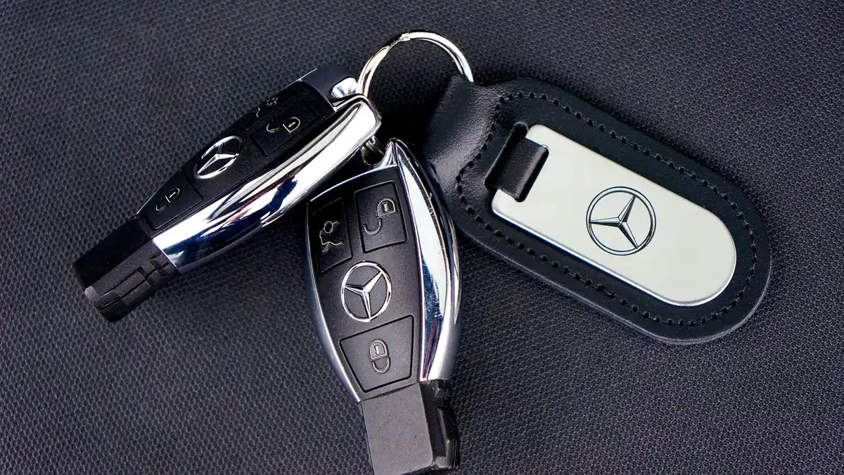 Two car key fobs and a leather key tag on a dark fabric surface, ready to be handed back at drop-off
