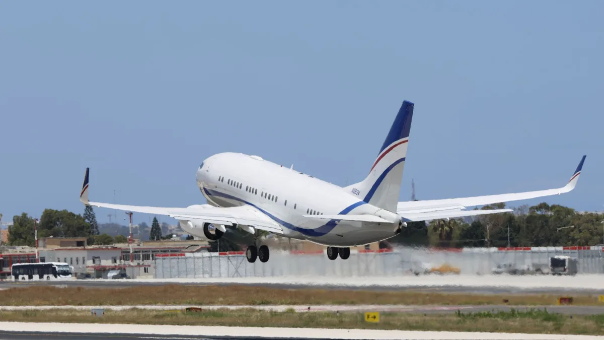 White passenger jet with a blue tail fin descending to land on an airport runway under a clear blue sky
