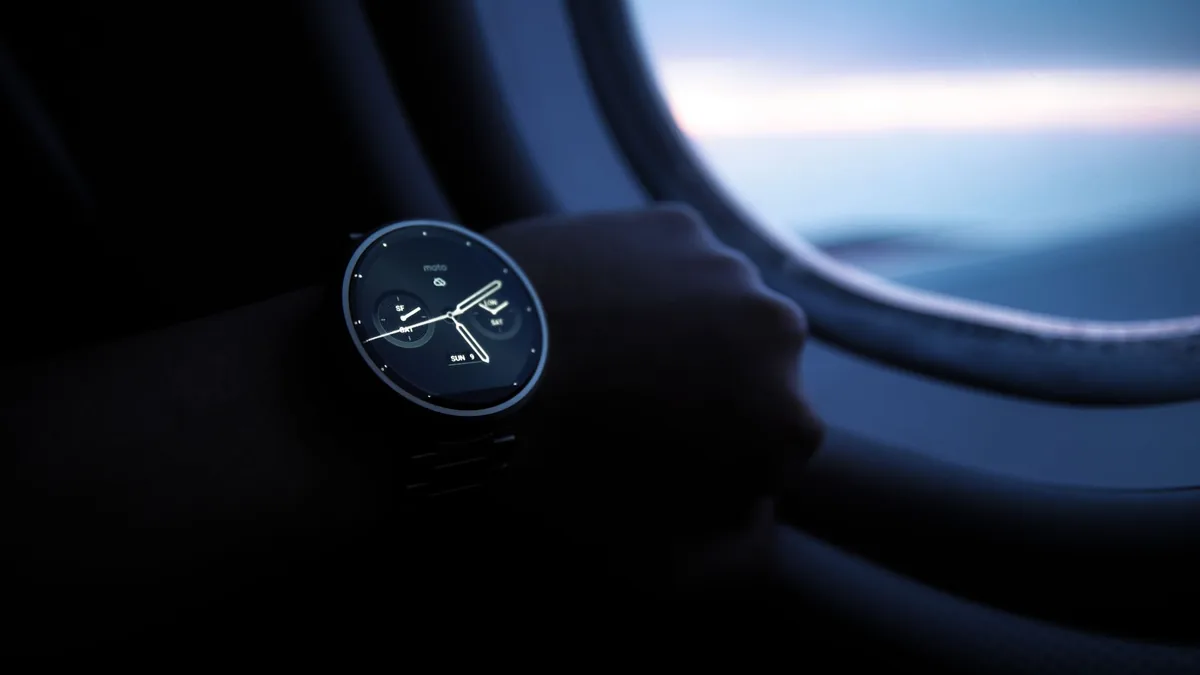 Smartwatch on a passenger's wrist beside an aircraft window with a pale sky outside during a flight