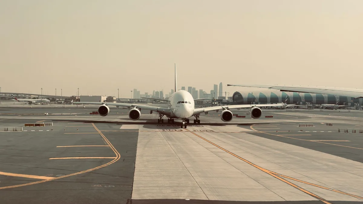 Wide-body A380 airliner taxiing on an airport apron in hazy light, with a city skyline on the horizon