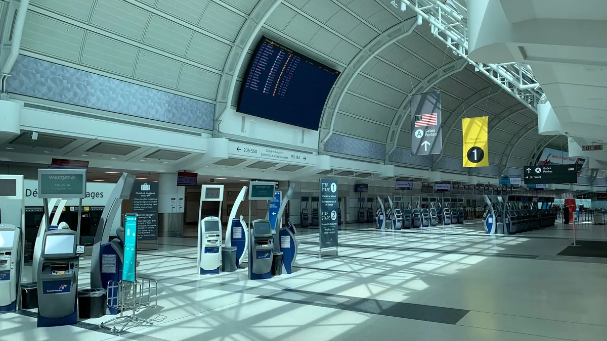 Bright, nearly empty airport departures hall with self check-in kiosks and a row of check-in counters under a curved roof