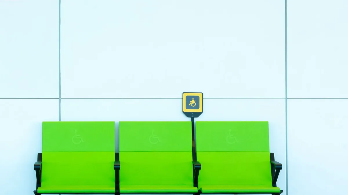 Row of bright green priority seats marked with wheelchair accessibility symbols against a pale blue wall