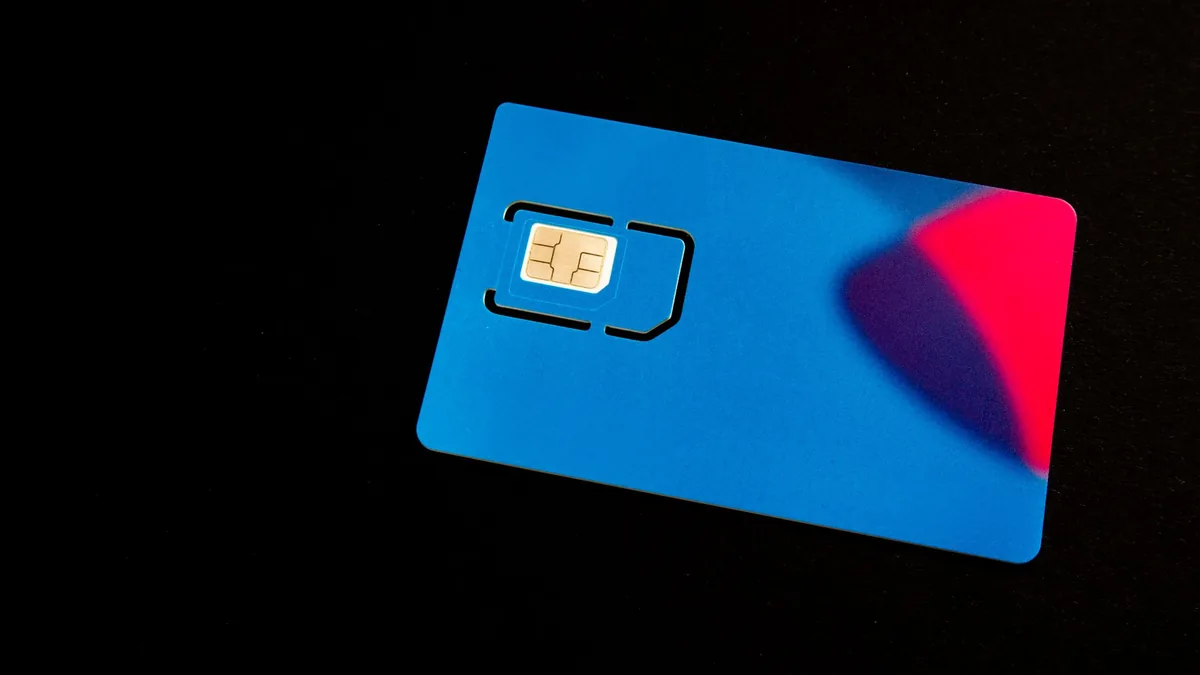 Close-up of a blank blue and red SIM card holder with the chip visible, lying on a plain black surface