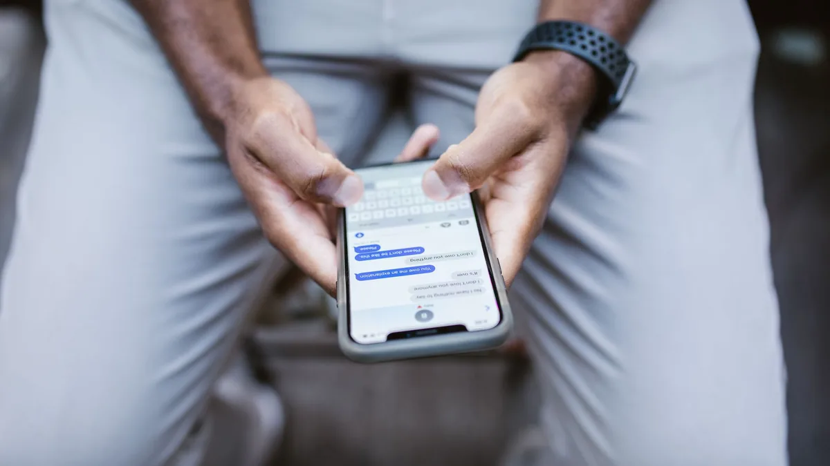 Close-up of a seated person's hands holding a smartphone with a messaging chat open on the screen
