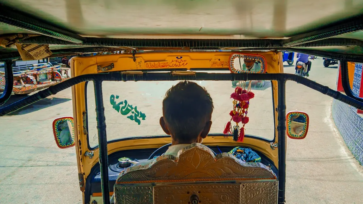 View from the passenger seat of a yellow auto rickshaw, driver seen from behind, looking out onto a sunny street
