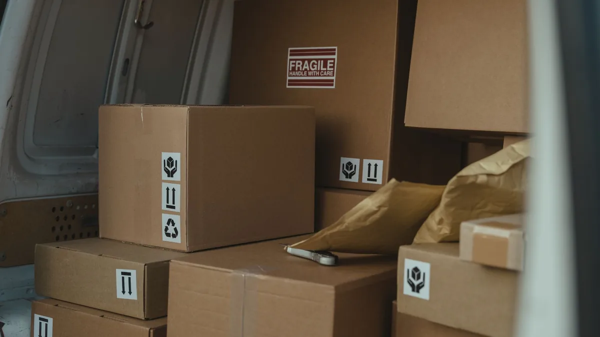 Sealed cardboard boxes marked fragile stacked in the cargo area of a van, with padded envelopes on top