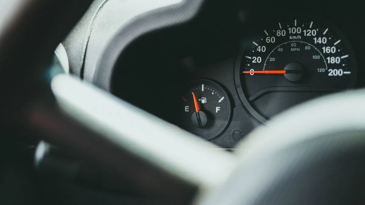 Car instrument cluster with a km/h speedometer and a fuel gauge needle low, seen past a blurred steering wheel