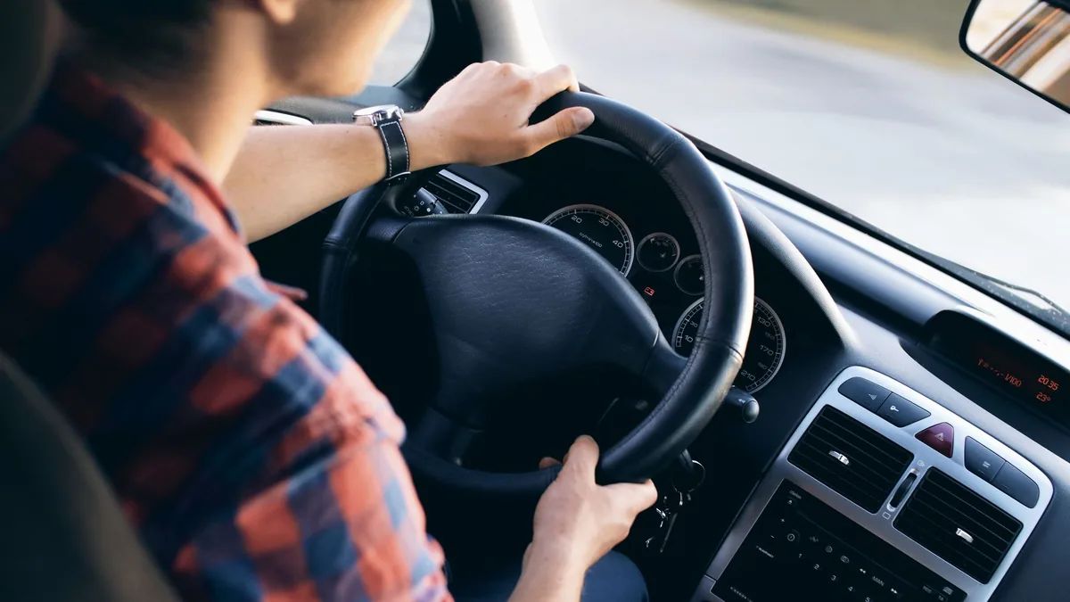 Driver in a checked shirt with both hands on the steering wheel of a right-hand-drive car, dashboard in view