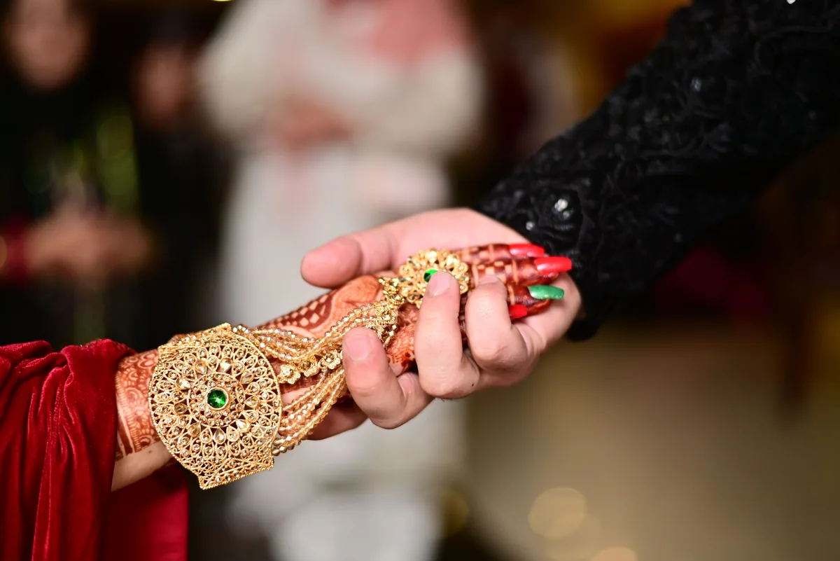 Joined hands with embroidered cuffs, henna and gold jewellery