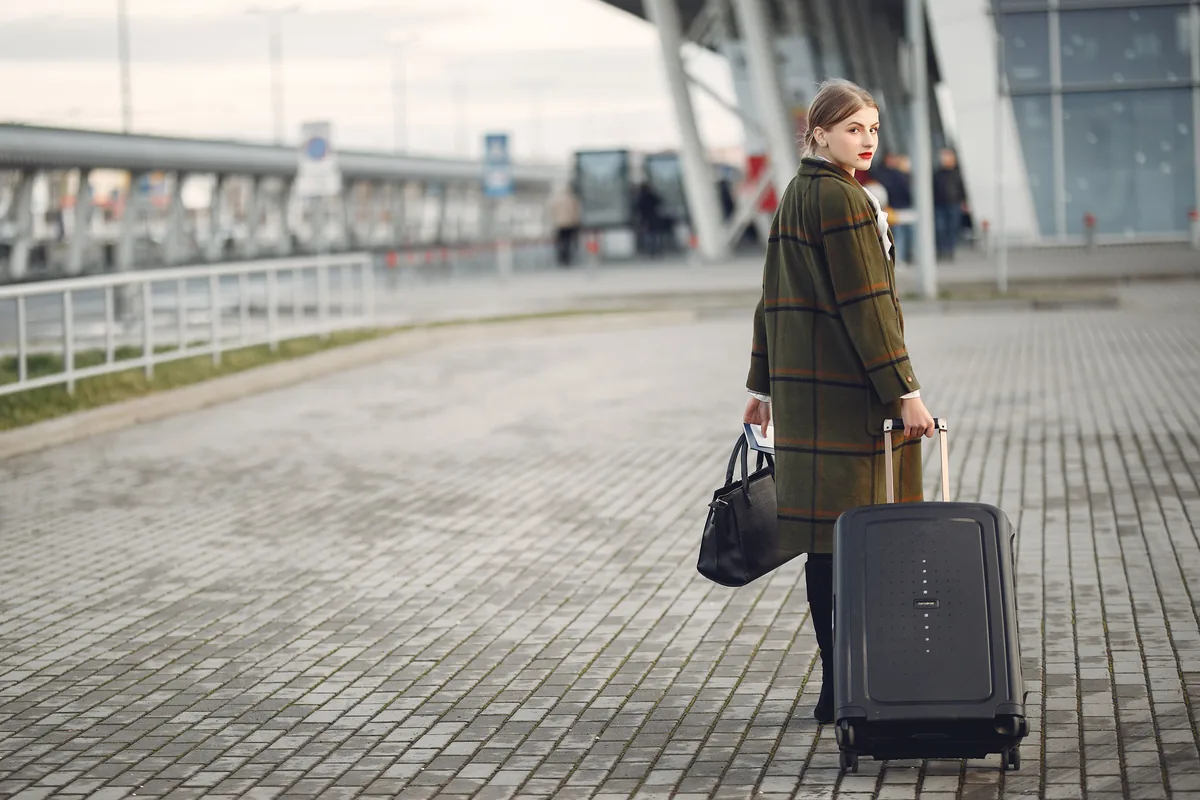 Traveller walking with a wheeled suitcase outside an airport
