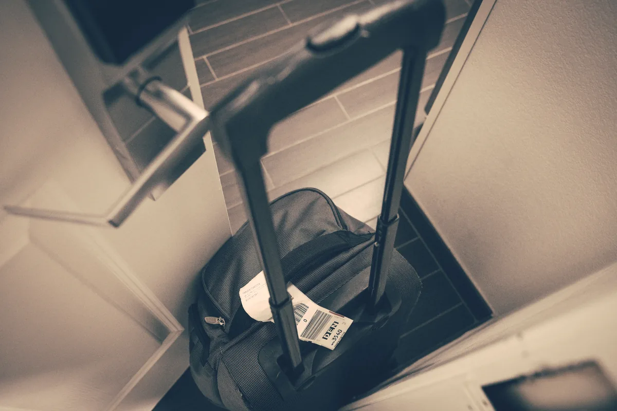 Suitcase at a doorway Dark wheeled suitcase with a travel tag beside a doorway