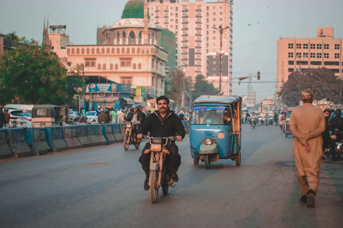 Rickshaws and motorcycles moving along an urban street