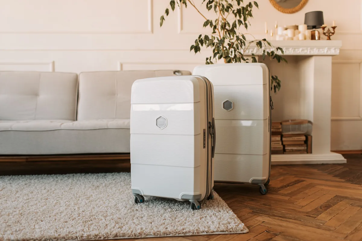 Two pale wheeled suitcases beside a sofa